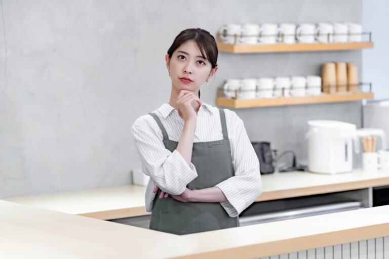 カフェで頭を抱えるエプロンをつけた女性