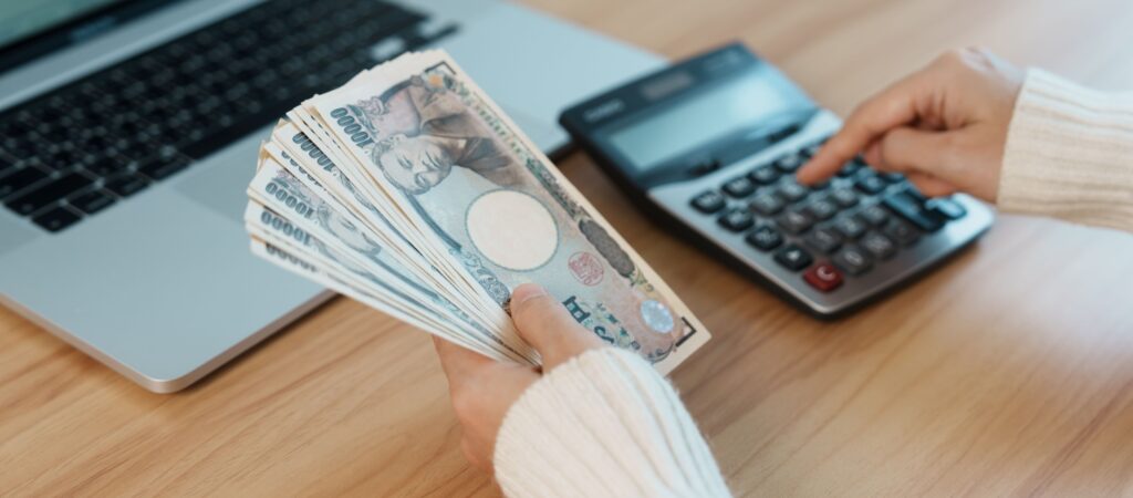 電卓を使って日本円の紙幣を数えている女性の手