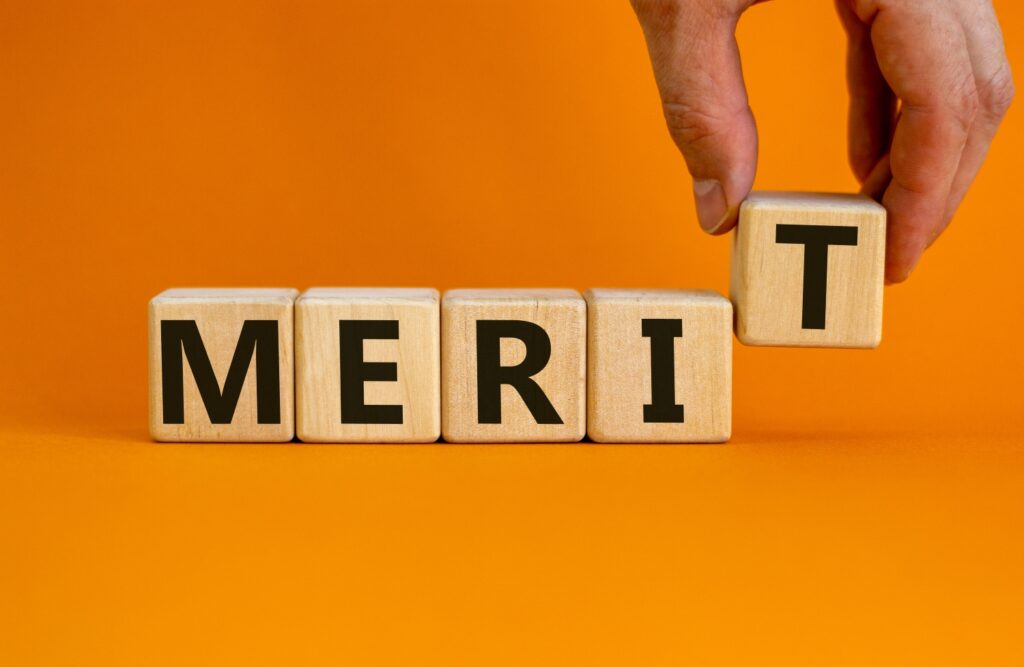 メリットを表すイメージ。「merit」の文字が並ぶ木製キューブとビジネスマンの手