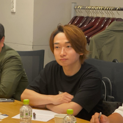 会議室のテーブルで、黒いTシャツの男性が腕を組み、横を向いている