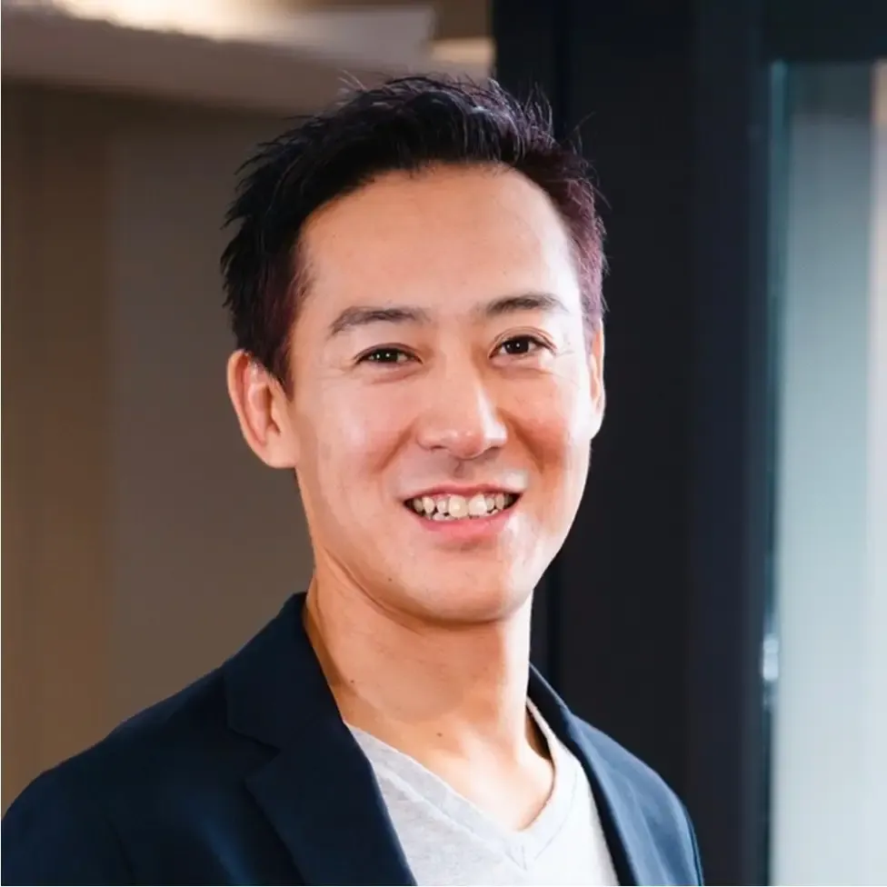 絶好調の代表取締役 吉田 将紀氏が、紺のジャケットに白いTシャツ姿で笑っている