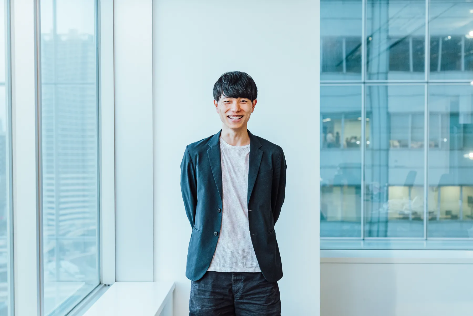 Dinii Inc. CEOのMao Yamadaが、紺のジャケット姿で窓際に立ち、笑顔を見せる