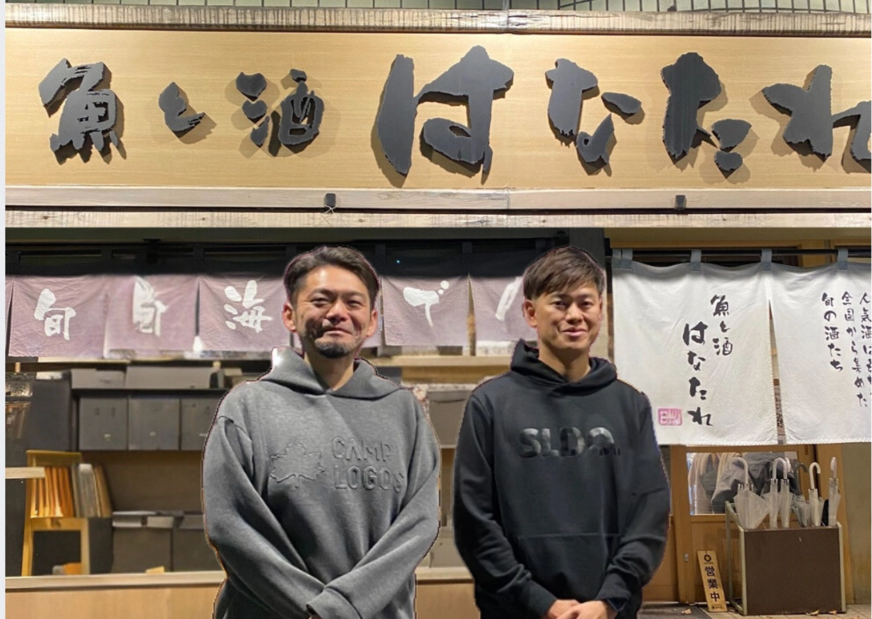 「魚と酒 はなたれ」の看板の前に、パーカー姿の男性2人が並んで立っている
